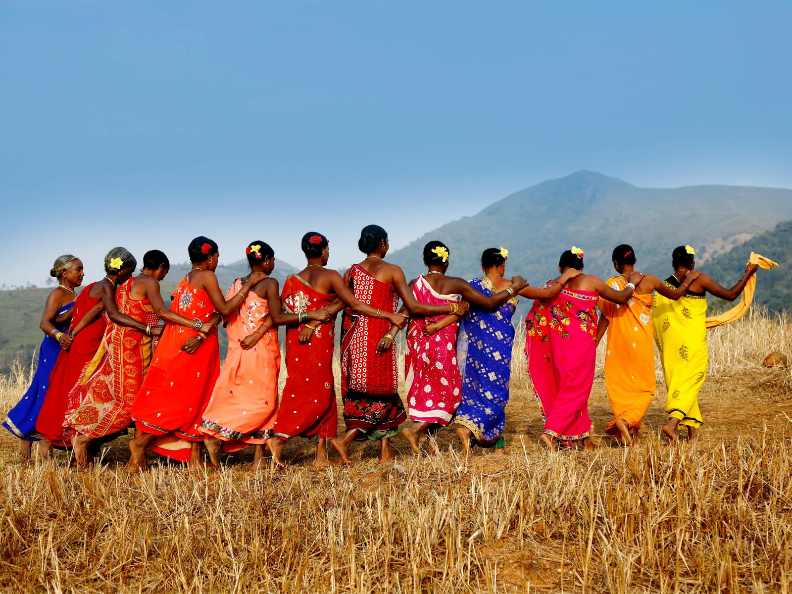 Women in bright saris dancing together in a dry field